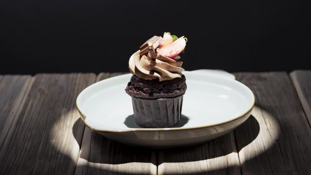 I put a plate with a cupcake on a wooden table, under a ray of light, berry and chocolate dessert.