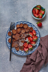 Mini chocolate pancake cereal with strawberries for breakfast on gray concrete table. Trendy home breakfast with tiny pancakes. Top view.