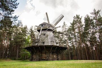 Old historic wooden windmill in Latvia, grey sky, rock base, green trees in the background