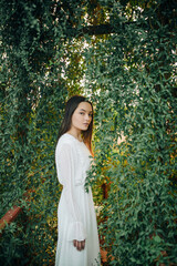 Woman stands on a bridge entwined with lianas in orangery.