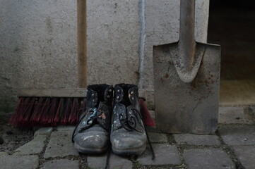 old worn painted work boots with a yard broom and a spade as symbol for cleaning, house keeper or...