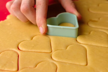 Making gingerbread cookies in heart shape using plastic cutter on the red silicon baking mat. Sweets for St. Valentines Day. 