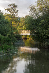 Fototapeta na wymiar OXFORDSHIRE, UK: Pretty wooden footbridge over small river with reflection