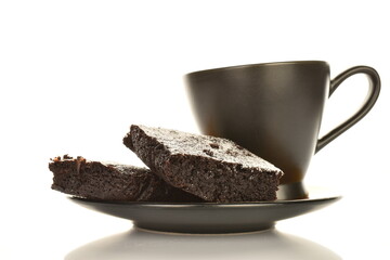 Two chocolate brownies with cherries on a saucer with a cup, close-up, on a white background.