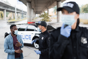 African american victim in medical mask standing near police officer and policewoman on blurred foreground on urban street.