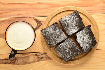 Several chocolate brownies with cherries on a wooden tray with a cup of milk, close-up, on a wooden table.
