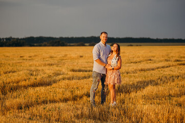 Naklejka na ściany i meble A happy couple in a field in the rays of the setting sun