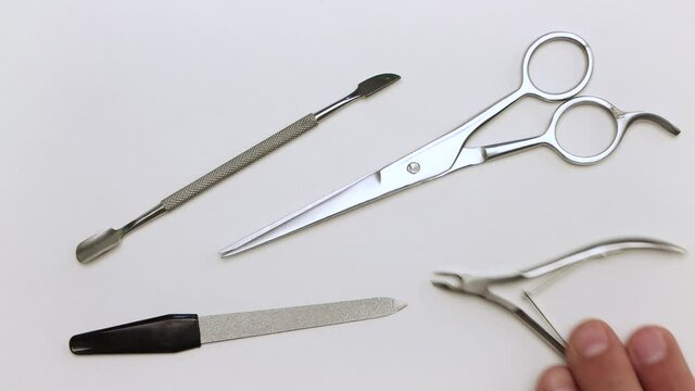 A man in close-up takes scissors, nippers, scraper and nail file. Demonstration of tools for manicure. Items for work on a light surface. Professional hand care. Isolated video on a white background.