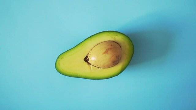 Avocado on a blue background. Half a rotating avocado on a isolated colored background. Looping food video 