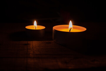 Two lighted tea wax candles on a wooden table on a black background