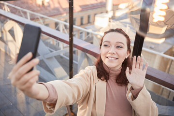 Young blogger smiling at camera recording video on her mobile phone for her blog