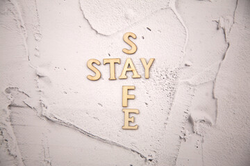 The word stay safe is made of wooden letters against a background of white plaster on a concrete wall