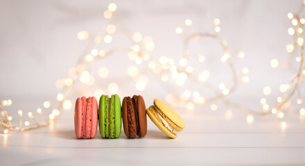 Multicolored French macaroons on a light background with a beautiful bokeh from a garland. Abstract background, selective focus
