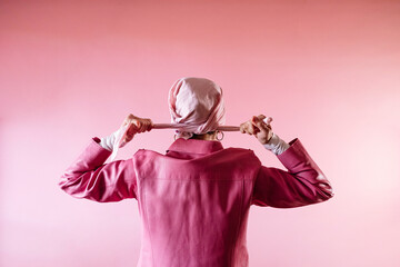 Woman from behind tying a pink scarf on her head, cancer patient. - obrazy, fototapety, plakaty
