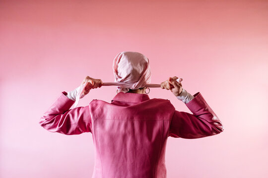 Woman from behind tying a pink scarf on her head, cancer patient.