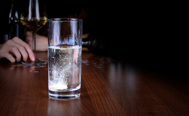 Glass with effervescent tablet on a dark background stock images. Effervescent tablet into a glass of water images. Hangover drink photo. Fizzy tablet in water on a black background with copy space