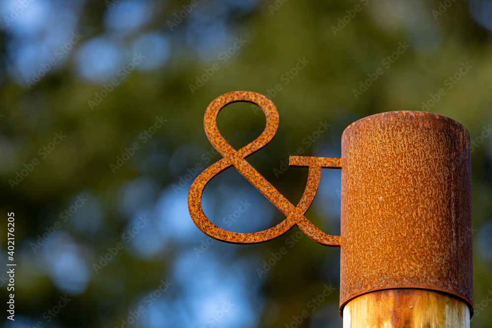 Wall mural Rusty rustic vintage 'and' symbol sign with out of focus blurred natural dark green with blue sky spots coming through background