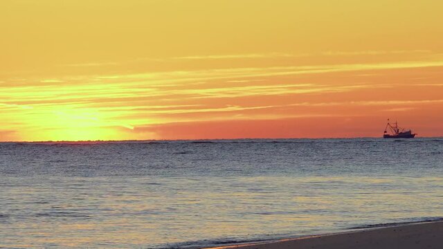 A shrimping boat sails on the horizon during sunrise at folly beach