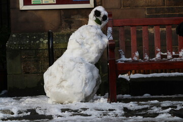 One Snowman Leaning on a Public Bench on the Pavement