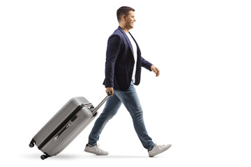 Full length profile shot of a young man smiling and walking with a suitcase