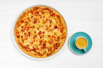 Cup of coffe and homemade pizza with meat, peppers, tomatoes and cheese on white wooden table. Top view.
