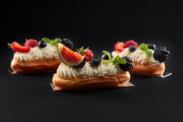 Homemade eclairs with cream and berries isolated on black.