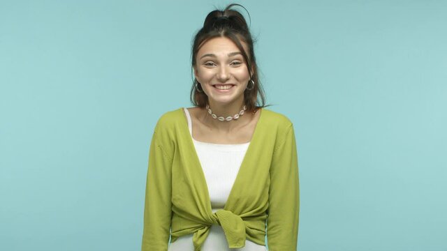Cute and humble girl raising eyebrows and smiling, shrugging shoulders shy, receive compliments or praises, feeling happy, standing over blue background