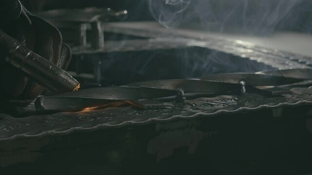 Forge workshop. Smithy. Worker in a welding hood helmet welds a part by electric welding. Sparks are reflected in the protective screen. Blacksmith makes iron product for manufacture. Slow motion.