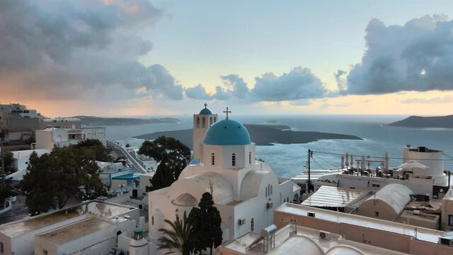 Aerial shot flying over a traditional church in Thera city, Santorini at sunrise
