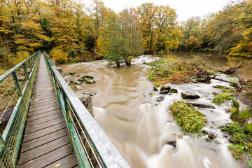 Passerelle piétons verte au-dessus d'une rivière en crue et boueuse en automne en pose lente. La...