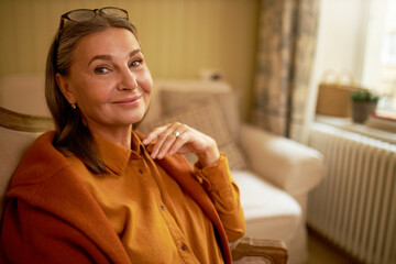 Close up image of beautiful positive woman pensioner wearing eyeglasses on her head and sweater on...