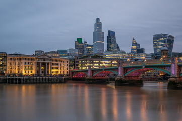 A view of the City of London, at dusk, from the south side of the River Thames, across Southwark Bridge.