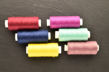 Several spools of colored thread, close-up, on a slate board.