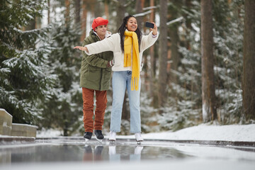 Young woman making selfie portrait on mobile phone while skating together with her boyfriend...