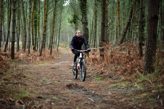 Beautiful Young Woman Mountain Biking In The Forest In Winter