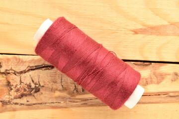 One spool of burgundy thread, close-up, on a wooden table.