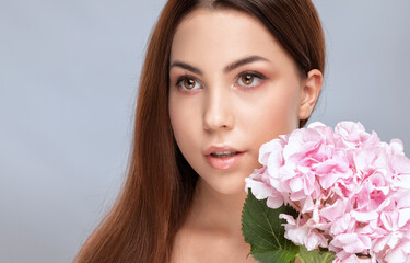 Portrait of a beautiful brunette woman with healthy clean skin and fresh make-up. She holds a pink...
