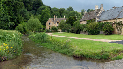 Fototapeta na wymiar GLOUCESTERSHIRE, UK: View along small stream and ford toward large stone house