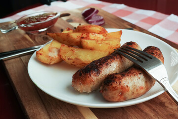 rustic potatoes and grilled sausages lie on a white plate that sits on a cutting board.