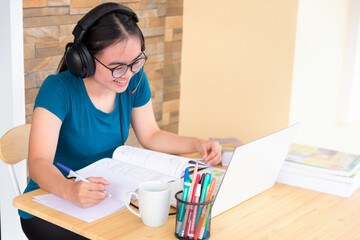 Young student Asian teenage girl with headphones and glasses is smiling happy looking at laptop computer online learning from school. Distance education class of the university video call at a home