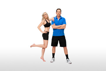 Portrait of a fit, young, white coach in a blue shirt & serene fit female athlete with curly long blond hair posing together in a studio with a white background wearing black shorts & sports bra.