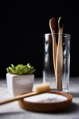 Bamboo toothbrushes in glass, baking soda and bathroom towels on dark background