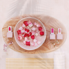 Preparation for a caring procedure in a manicure salon. Jars of nail Polish and a bath of nourishing water with rose petals on a pink table. Cosmetics mock up for manicure branding. Square orientation