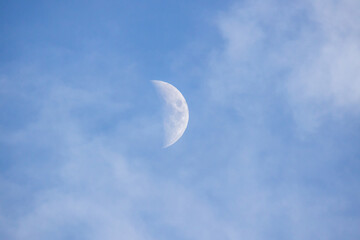 Crescent moon over blue sky with high clouds at sunset.