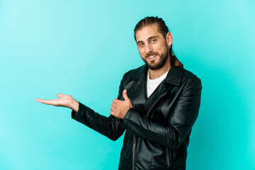 Young man with long hair look showing a copy space on a palm and holding another hand on waist.