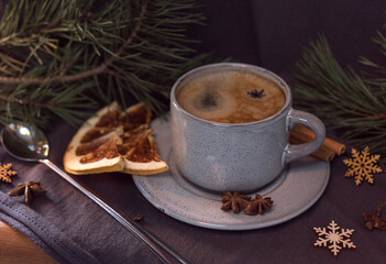 a cup of black coffee with froth on a background of pine branches, orange slices, New Year's toys, cinnamon
