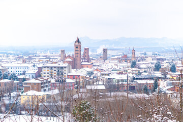 Obraz premium View of small medieval Alba town and vineyards on the hills covered in snow in Piedmont, Northern Italy. Langhe wine truffle region. 