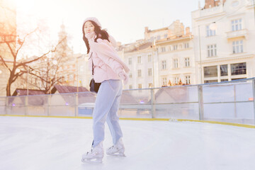 Happy asian woman going to ice skating outdoor. Korean female dressed in powder pink jacket and warm knitted hat. Holding. Healthy lifestyle and sport concept at city square. Winter weather at sunny d