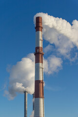 Smoking chimneys against the blue sky.Thick white smoke spreads across the sky. Long red and white...