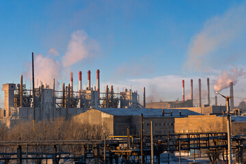 Industrial landscape. Smoking chimneys of a factory on a background of blue sky. Rows of pipes....